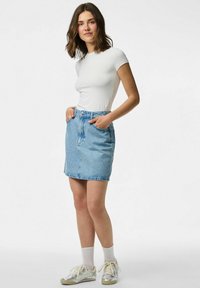 Heledanikkatiseed sinise pesu tooniga, millel on esiküljel taskud, nööbid ja väikesed dekoratiivsed detailid, koos valge t-särgi ja tennisekingadega.