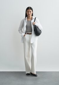 Balta krekla ar garām piedurknēm pār pelēku ribotu augšu; augstās vidukļa krēmkrāsas bikses; melni ādas dzīvokļi; austs melns rokassomiņa; minimālistisks dizains.