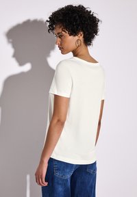 Kortærmet, cremefarvet t-shirt lavet af blødt stof, med rund halsudskæring og afslappet pasform. Kombinationen med blå denim jeans.