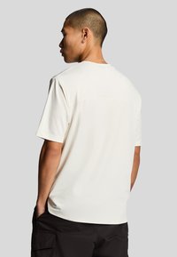 Kortærmet cremefarvet T-shirt lavet af blødt stof, med rund hals og sømløst bagdesign, båret med sorte cargo shorts.