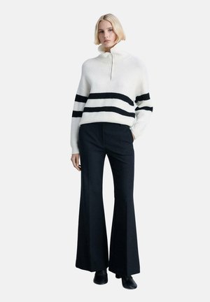 White knit sweater with black horizontal stripes, collar with half-zip, paired with black flared trousers and ankle boots.