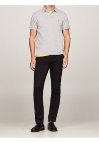 Polo gris à manches courtes, associé à un pantalon noir ajusté. Des chaussures de ville noires complètent la tenue, avec un sous-vêtement jaune.