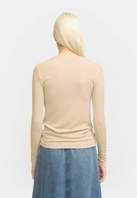 Beige long-sleeve fitted top with a scoop neckline, paired with a denim skirt. The top has a smooth texture and a subtle ribbed pattern.