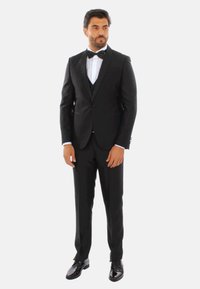 Tuxedo nero con rever in raso, camicia bianca e papillon. Pantaloni slim-fit e scarpe nere lucide completano il look formale.