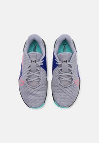 Scarpe sportive grigie con una tomaia in mesh, caratterizzate da accenti blu, uno swoosh rosa e una suola texturizzata. I lacci sono grigi con un’etichetta sul linguetta.