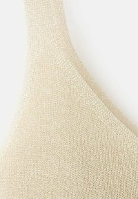 Svetlo bež pleten modrček z gladko teksturo in širokim, ukrivljenim trakom, ki prikazuje nežno, sijočo površino.