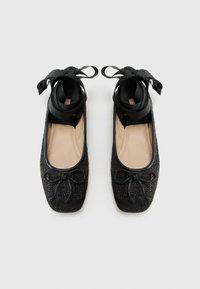 Ballerines noires en tissu doux, avec un accent de nœud, des rubans en satin et un motif décoratif en sequins sur la surface supérieure.