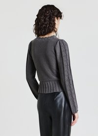 Dunkelgrauer gestrickter Pullover mit Puffärmeln, rippenförmigem Saum und Zopfmusterakzenten an den Ärmeln. Kombiniert mit schwarzen Lederhosen.