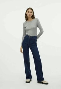 Grå langermet topp og mørkeblå høyt midje jeans. Jeansene har en tettsittende midje og rette ben, laget av denim med en glatt tekstur.