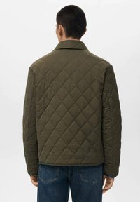 Gequilted olijfgroene jas met een kraag, met een boxy vorm en zichtbaar ruitpatroon. G gedragen met blauwe jeans, die een relaxte fit tonen.