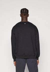 Felpa nera con scollo rotondo, polsini e orlo a costine, spalle scese e un piccolo logo a stella bianca sul retro. Tessuto morbido.