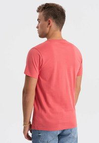 Koralfarvet kortærmet t-shirt lavet af blødt bomuldsstof med rund hals, vist fra ryggen, der viser et enkelt design og pasform.