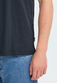Camiseta de algodón negra con escote redondeado. Incluye una etiqueta lateral. Combinada con unos vaqueros de mezclilla azul claro con una textura desvanecida.
