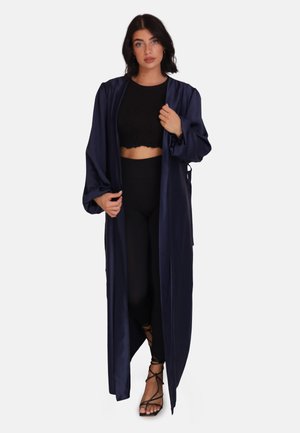 Robe longue en satin navy avec de larges manches, design légèrement drapé et fermeture à nouer. Associée à un crop top noir et un legging ajusté.