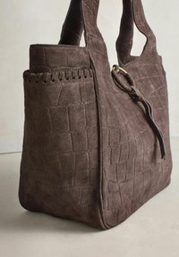 Pruun seemisnahast kandekott tekstureeritud ruudumustriga, laiade sangadega ning küljes dekoratiivse rõnga ja nahast paelaga.