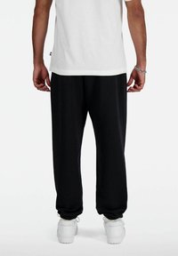 Schwarze Sweatpants mit elastischen Bündchen, aus weichem Stoff. Kombiniert mit einem weißen T-Shirt und weißen Sneakern, die einen lässigen Look zeigen.