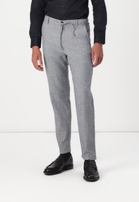 Ljust grå byxor i en texturerad tyg, med resårmidja och dragsnodd, stylad med svarta skor och en figursydd svart skjorta.