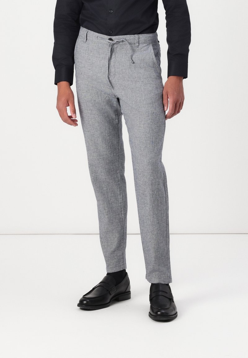 Ljust grå byxor i en texturerad tyg, med resårmidja och dragsnodd, stylad med svarta skor och en figursydd svart skjorta.