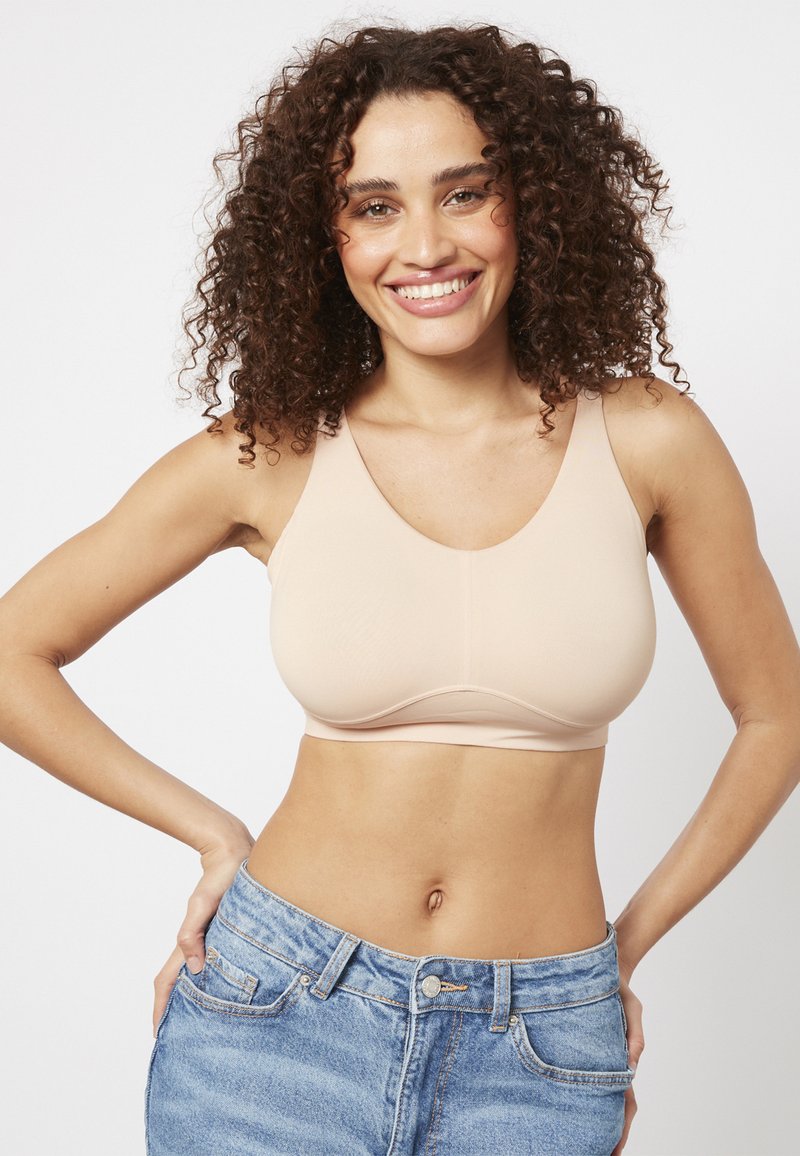 Senza cuciture, reggiseno beige con scollatura a V e spalline larghe. Texture liscia, coppe sagomate, con hardware minimale e senza cuciture visibili.