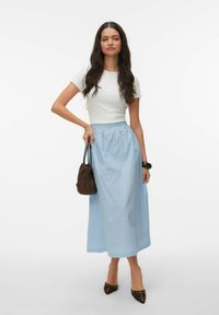 Lyseblå maxinederdel med elastisk talje, kombineret med en tætsiddende hvid t-shirt. Tilbehør omfatter en lille brun taske og spidse hæle.