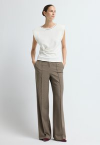 Biała bezrękawnikowa bluzka z dekoltem w łódkę i marszczeniem, w połączeniu z brązowymi, w kratkę szerokimi spodniami i burgundowymi czółenkami.