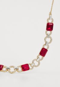 Zelta krāsā savienots kaklarota ar taisnstūra sarkaniem akmeņiem un apļveida rhinestone akcentiem, ko savieno apļveida un taisnstūra metāla formas.