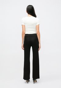 Pantalon noir en maille évasé à taille haute, associé à une chemise blanche ajustée à manches courtes ; texture lisse et coupe cintrée.