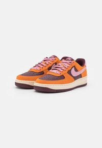 Nike-sneakers med orange mocka, mörkbruna detaljer, rosa snören och en beige mellansula med texturerad gummiyttersula.