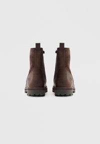 Botas de cuero marrón y ante con un acabado suave, de altura hasta el tobillo, con lengüetas para tirar y suelas de goma resistentes visibles en la vista trasera.