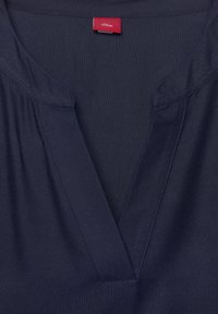 Navy blue lyhythihainen paita V-kaula-aukolla, kevyt kangas, yksinkertainen ommelkoristelu ja punainen brandilogo kaulan sisäpuolella.