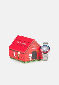 Zegarek Timex z niebiesko-czerwonym pierścieniem, stalową bransoletą i czarną tarczą, zapakowany w czerwoną kartonową budę dla psa z postaciami z Peanuts.
