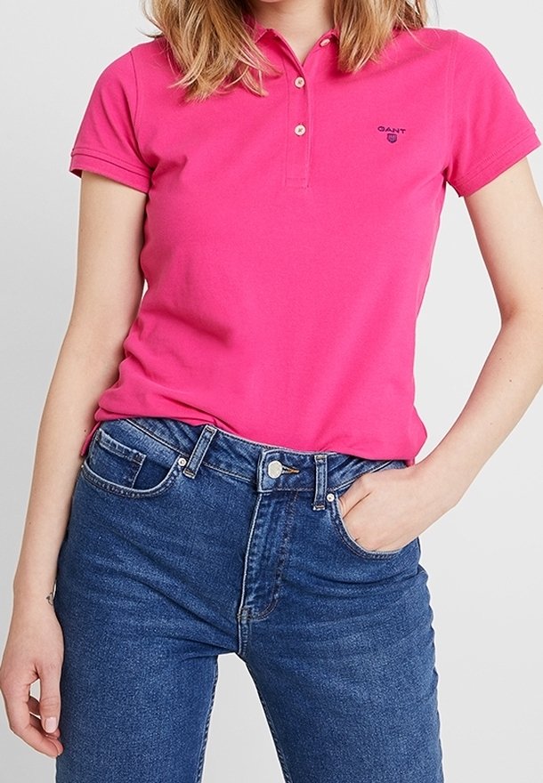 Fitted pink Poloshirt mit einer Dreiknopfleiste und kleinem Logo auf der linken Brust, kombiniert mit dunkelblauer Denim-Jeans.