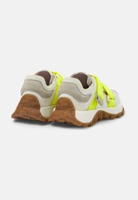 Sneaker mit grauem Wildleder und weißem Synthetik-Obermaterial, hervorgehoben durch einen neon-gelben Riemen, mit einer strukturierten braunen Gummisohle.