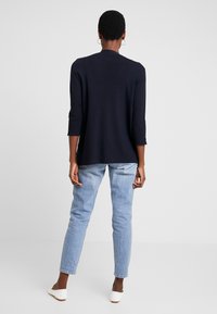 Camiseta de manga larga azul marino con escote redondo, ajuste relajado y mangas de longitud media, combinada con jeans de mezclilla azul claro y zapatos blancos.
