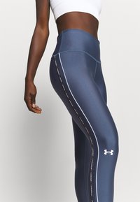 Legginsy w kolorze granatowym z wysokim stanem, o gładkiej fakturze, z białymi paskami po bokach i logo Under Armour. Elegancki design do odzieży sportowej.
