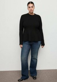 Maglione nero a coste con maniche lunghe e silhouette a peplum, abbinato a jeans svasati blu scuro e scarpe nere.