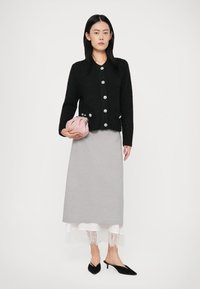 Svart strikket cardigan med store sølvknapper, grå skjørt, hvit blondekant, myk rosa clutch-veske og svarte spisse mules.