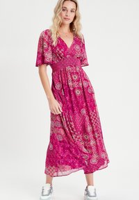 Robe rose à motifs avec un décolleté en V, des manches courtes évasées, une taille froncée et une jupe fluide. Portez-la avec des baskets blanches et grises.