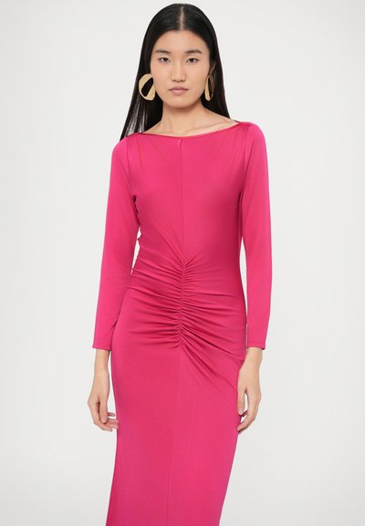 Hosszú ujjú, élénk rózsaszín ruha, amely deréknál összegyűrt, ráncolt kialakítással rendelkezik, csónaknyakú kivitelben. A modellen nagy, kerek fülbevalók láthatók.