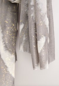 Sciarpa grigia e bianca con una texture morbida a motivo spina di pesce, arricchita da pagliuzze dorate e bordi sfrangiati.