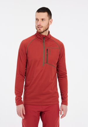 Pullover rosso a maniche lunghe con colletto alto, chiusura a zip frontale e cuciture di accentuazione verdi. Ha una tasca con zip sul lato sinistro del petto. Tessuto testurizzato.