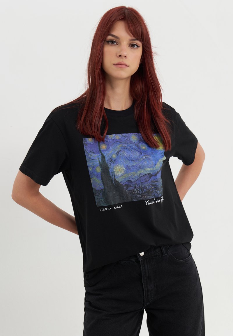 T-shirt noir avec une impression encadrée de "La Nuit étoilée" de Vincent van Gogh. Manches courtes, col rond et coupe décontractée.
