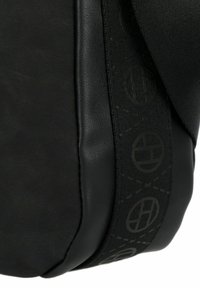 Borsa in pelle nera con superficie texturizzata, dotata di una tracolla nera a fantasia con accenti circolari. La forma curva sottolinea un design compatto.