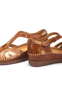 Sandali in pelle marrone con finitura testurizzata, dotati di dettagli a intaglio, cuciture a contrasto e cinturini regolabili per una vestibilità sicura.