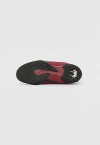 Scarpa sportiva rossa e nera con suola in gomma testurizzata. Presenta una parte superiore liscia con aree in mesh, un design slanciato e un logo sul tallone.