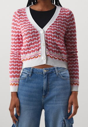 Cardigan a bottone in rosa e bianco, con un motivo testurizzato e polsini a costine, abbinato a jeans in denim blu.
