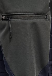 Mörkgrå funktionsväv med en dragkedjeförsedd ficka med svart dragkedja, slät textur och kontrasterande marinblå accenter på sidan.