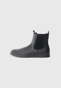 Botas Chelsea negras de material sintético liso, con paneles laterales de malla, lengüetas de agarre y suela de goma plana.
