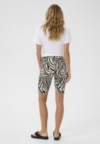 Zebra print fietsshorts van beige en zwarte stof, halverwege de dij, gecombineerd met een wit t-shirt en zwarte sandalen, gezien vanaf de achterkant.