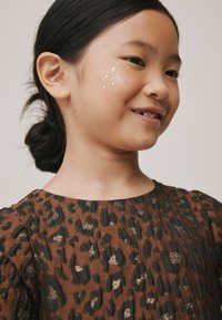 Barna tigrismintás ruha fekete díszítésekkel és fémes arany részletekkel. Sima szövetű, kerek nyakkivágással és felfújt ujjakkal.